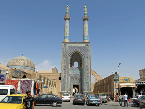 Yazd - Die Jame-Moschee (Freitags-Moschee) ist die große Versammlungsmoschee der Stadt Yazd. Sie wurde zwischen 1324 und 1327 an der Stelle eines früheren Feuertempels und einer seldschukischen Moschee begonnen. Sie wurde von Seyed Rokn od-Din, der aus wohlhabender Yazd-Patrizier-Familie stammte, finanziert. 1365 wurde sie erweitert und ist heute eines der herausragenden Gebäude des 14. Jh. im Iran. Die Moschee wird von einem Paar Minaretten gekrönt, den höchsten im Iran (48 m). Die Fassade des Portals ist mit blendenden Fliesen, hauptsächlich in blau, dekoriert. Innerhalb der Moschee befindet sich ein langer, mit Arkaden versehener, Hof (Sahn). Hinter einem tiefliegenden Iwan (Halle) befindet sich eine Altarkammer, ein durch ein Belüftungssystem gekühlter Raum. Diese Kammer unter der gedrungenen gefliesten Kuppel ist dekoriert mit Fayence-Mosaiken und ihr hoher Fayence-Mihrab (Gebetsnische, die die Gebetsrichtung anzeigt) aus dem Jahr 1365 ist einer der schönsten seiner Art.